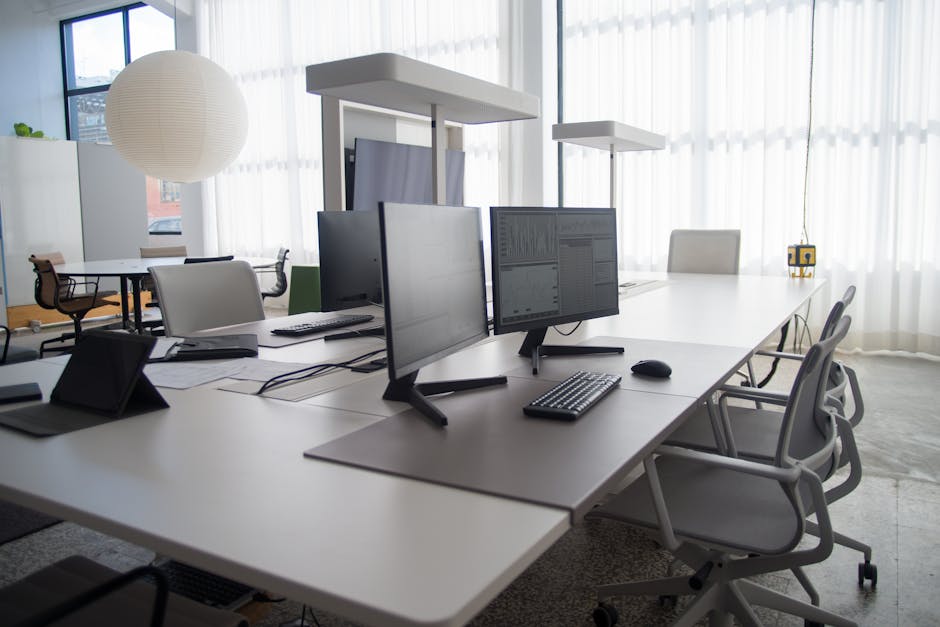 Spacious modern office featuring multiple computers, chairs, and collaborative workstations in natural light